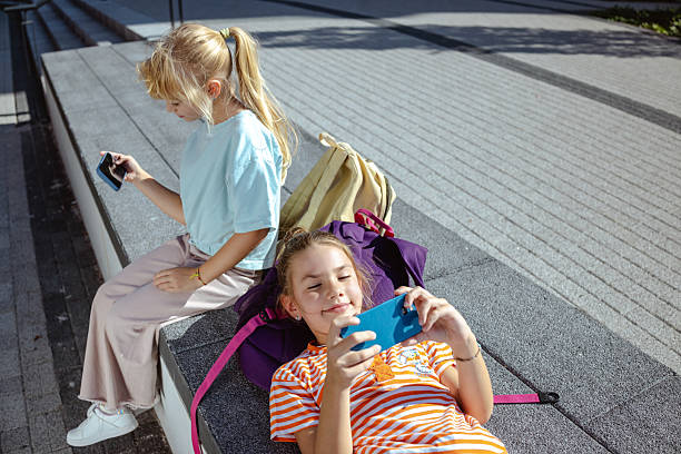 istock Two children using smartphones while sitting outdoors on sunny day 2217809683