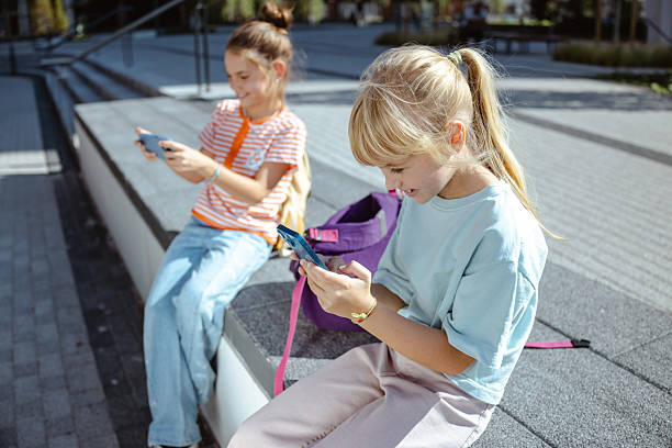 istock Two girls sitting outdoors using smartphones on a sunny day 2217809686