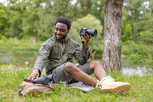 istock Young man enjoying bird watching in a lush forest by the water while holding a camera and exploring nature's beauty 2217809726