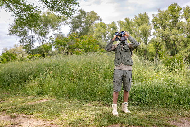 A young man is engaged in birdwatching, holding binoculars while exploring the beauty of nature in a verdant outdoor setting. He enjoys the freedom of this active lifestyle.