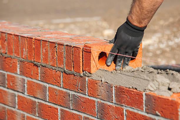 istock Close-up of skilled bricklayer working on construction site laying red bricks for wall construction while 2217812978
