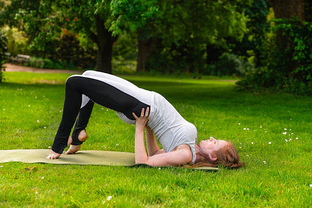 istock Woman practicing bridge pose in a green park during a sunny day, showcasing flexibility and strength in a peaceful outdoor setting 2217819639