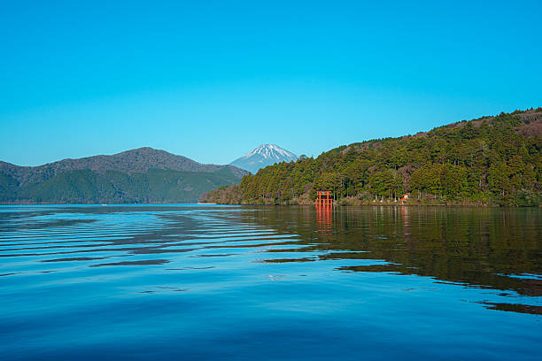 Hakone, Japan - Dec 10, 2023: Peaceful morning scene in Hakone, Japan, featuring Lake Ashi, a red torii gate, forested hills, and majestic Mount Fuji. The japanese text on the torii gate translate to Kuzuryu Shrine.