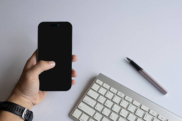 Person using smartphone at modern workspace with keyboard and pen on white background. Flat lay digital lifestyle concept for productivity.