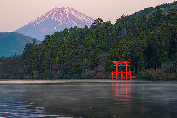 Hakone, Japan - Dec 10, 2023: Scenic view of Mount Fuji behind lush forest and iconic red torii gate at Lake Ashi in Hakone, Japan during sunrise. The japanese text on the torii gate translate to Kuzuryu Shrine.