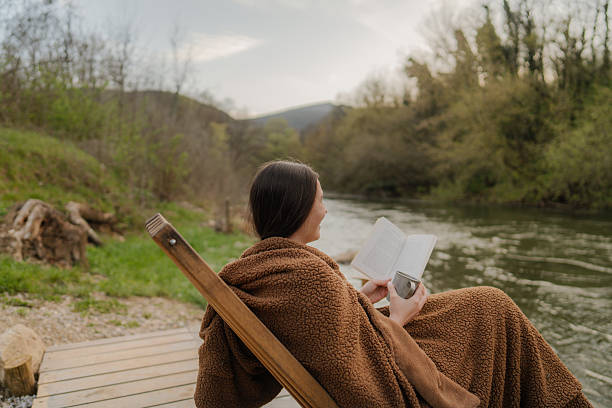 Photo of a young woman reading, soaking the sun and relaxing on a riverside dock