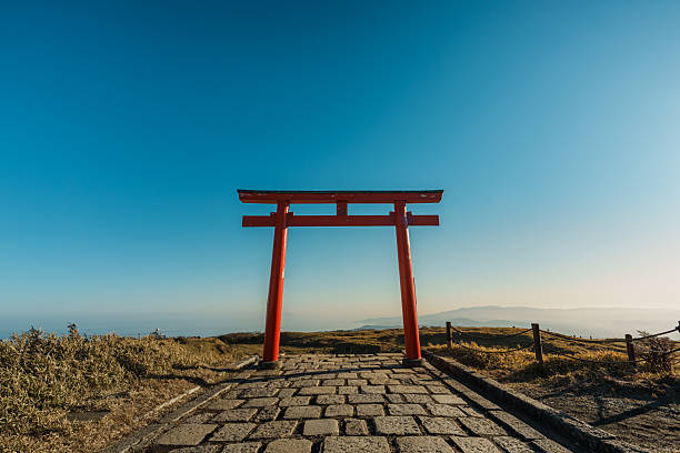 Hakone, Japan - Dec 10, 2023: A vibrant red torii gate stands at the start of the stone-paved path leading to the Hakone Mototsumiya Shrine, surrounded by golden fields.