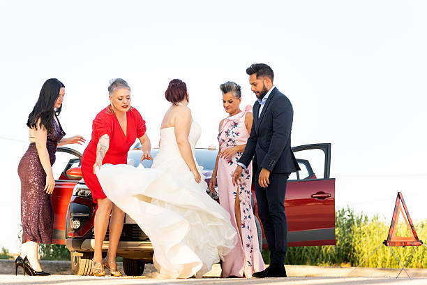 Bride, groom, and guests are fixing a problem with their car on the side of the road during a wedding