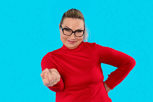 istock Smiling woman in a red sweater poses playfully against a bright blue background while holding a small gesture to indicate 'money' 2217829862