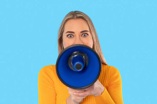 istock Woman holding megaphone and looking directly into the camera against a solid blue background during a vibrant and energetic moment 2217830235