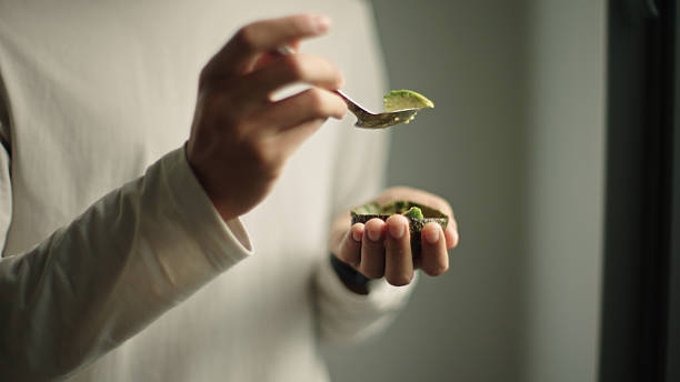 Asian man eating fresh avocado with a spoon by the window.