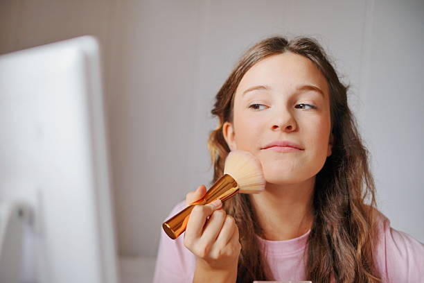 istock Adorable girl applying makeup with a brush in a bright, modern room while preparing for a special occasion 2217833851
