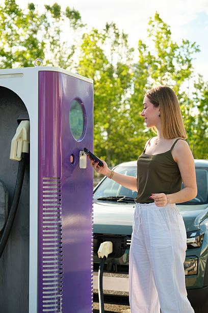 istock Young woman charging electric car using smartphone at charging station 2217833985