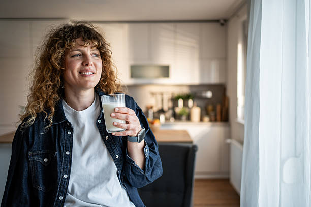 istock Smiling woman drinking milk in kitchen and looking out window 2217834197