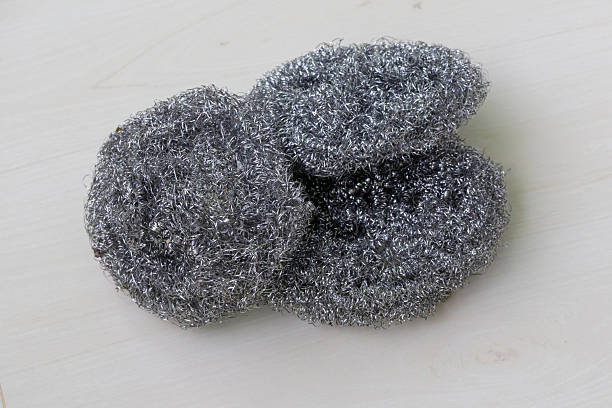 Three stainless steel dishwashing scrubbers on a light wooden surface.