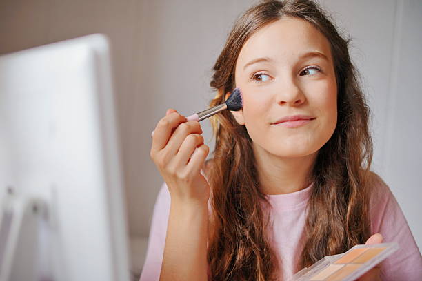 istock Girl applying blush while looking in the mirror at home, bright natural light highlighting her adorable features and creativity 2217835775