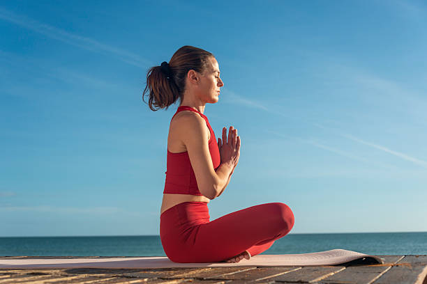 istock Woman Practicing Meditation in Lotus Pose by the Ocean on a Sunny Day 2217837100