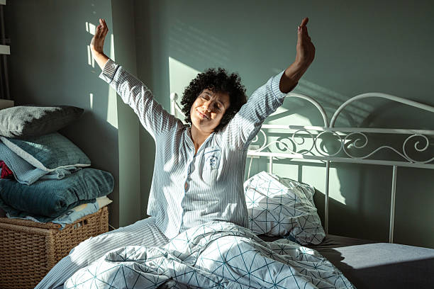 istock Woman stretching in bed with sunlight streaming through the window 2217841261