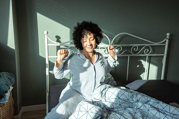 istock Woman stretching in bed with sunlight streaming through the window 2217841386