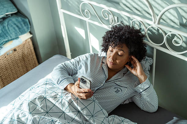 istock Woman in pajamas looking at her phone while lying in bed 2217842061
