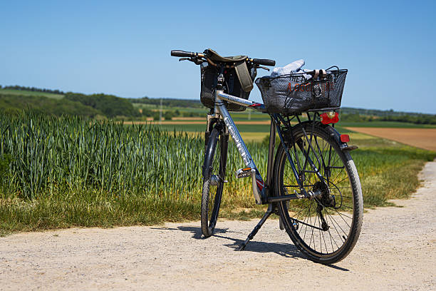 Wurzburg, Germany, May 27th, 2023. A fully loaded touring bicycle with handlebar and rear baskets rests on a gravel path through lush farmland under a clear blue sky.