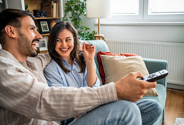 istock Couple watching tv and laughing together on sofa at home 2217845101