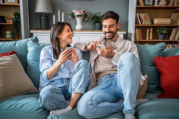 istock Young couple relaxing on sofa, using smartphones and laughing together 2217845488
