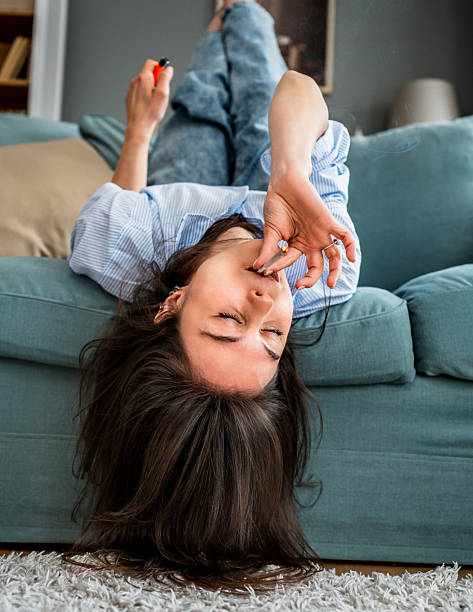 istock Young woman lying upside down on sofa smoking marijuana joint and having fun 2217846175