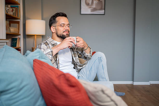 istock Young man relaxing on sofa, enjoying a cup of coffee at home 2217850984