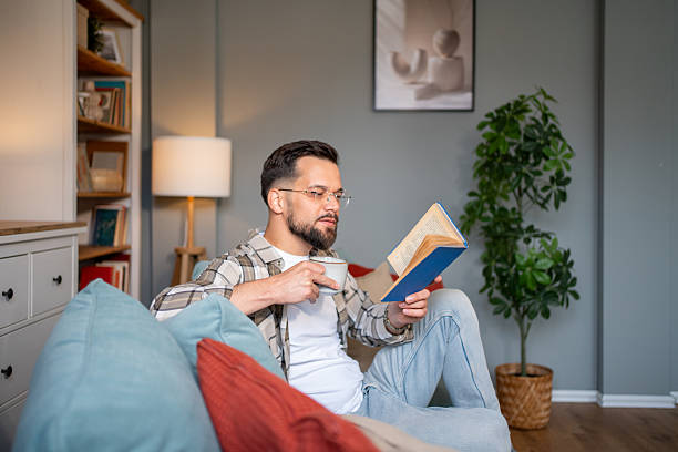 istock Young man reading a book and drinking tea on the sofa at home 2217850990