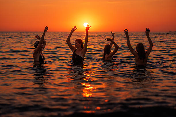 Four young women having fun and enjoying a seaside sunset on a vacation at the tropical beach.