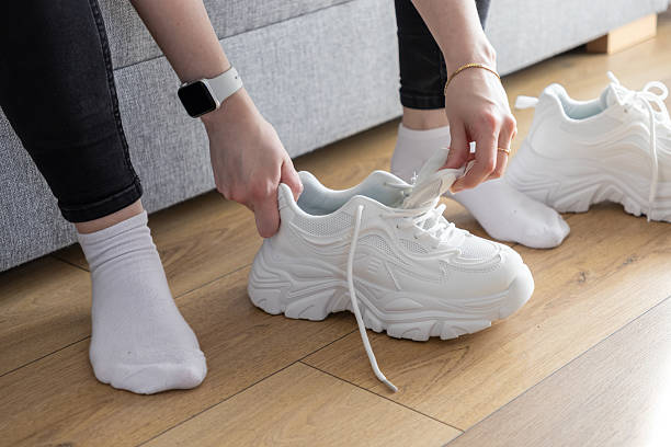 istock Person's hands pulling tongue of white chunky training sneakers indoors, illustrating preparation for comfortable exercise session 2217858977
