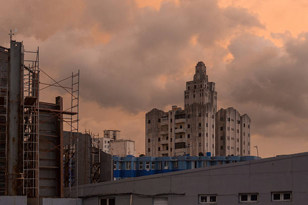 An art deco style building in Havana, Cuba, captured at sunset with a dramatic cloud-filled sky. The scene includes scaffolding and surrounding urban architecture, highlighting a blend of historical and modern elements.