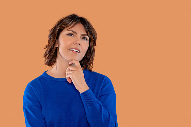 istock Curious woman contemplating ideas with a thoughtful expression against a solid orange background during a studio session 2217861844