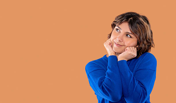 istock Woman with thoughtful expression poses with hands on cheeks against a warm brown background showcasing contemplation and creativity indoors 2217861928