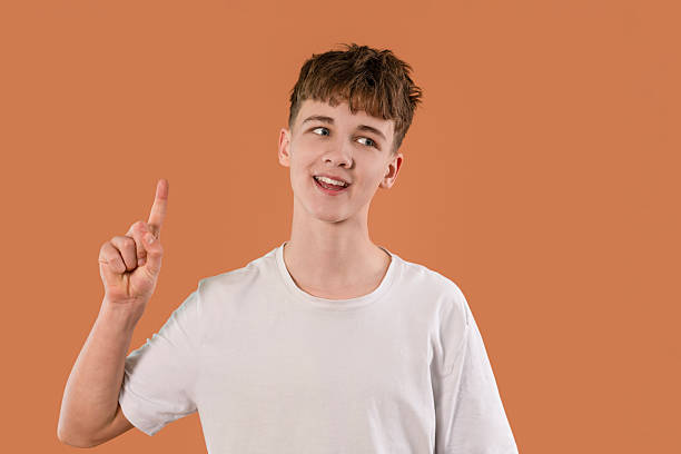 istock Young boy smiling and gesturing with a finger raised against an orange background during a fun moment of discovery 2217862639