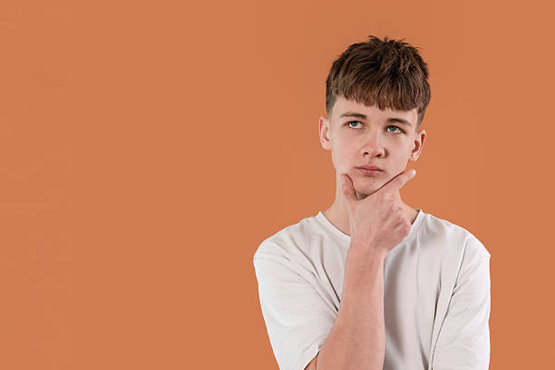 istock Boy thinking thoughtfully in front of an orange background during a creative brainstorming session in a studio 2217862946