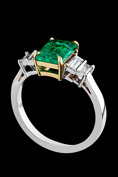 silver or gold ring with emerald stone and diamonds on black background close-up