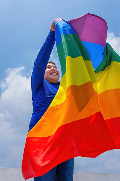 istock Young boy holding progress pride flag celebrating identity under blue sky 2217870316