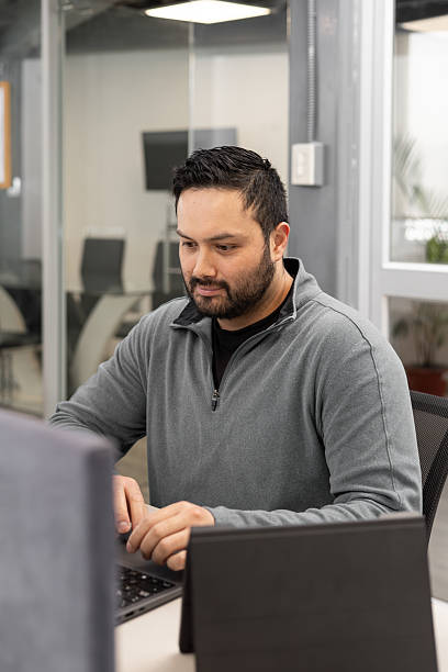 istock Bearded man in gray jacket looking at laptop with thoughtful gaze, surrounded by soft light in a quiet workspace 2217875783