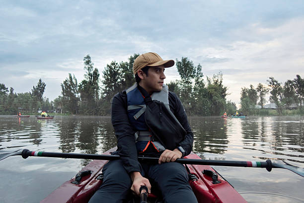 Paddling through tranquil waters, a person enjoys an early morning kayaking experience. Surrounded by nature, the still lake reflects soft hues of dawn while other kayakers engage in this peaceful outdoor activity.