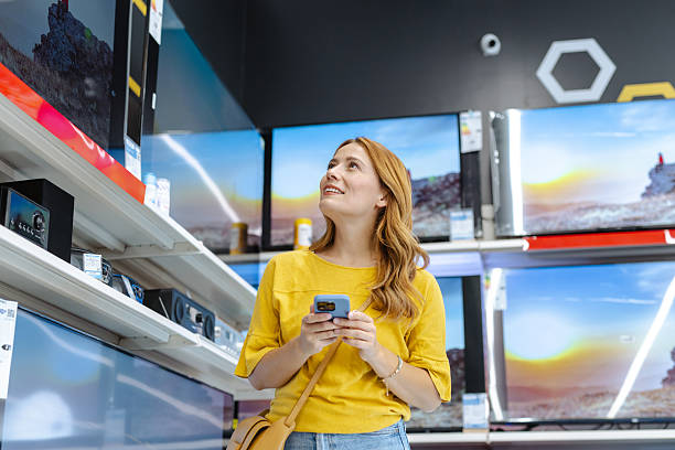 istock Woman selecting a television while referencing her smartphone in an electronics store 2217880488