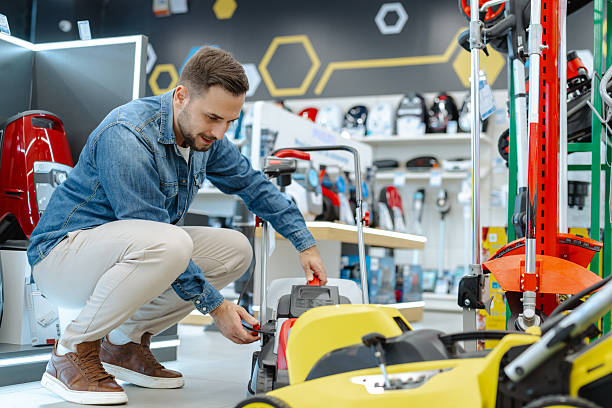 A man browsing a selection of modern lawn mowers in a well-equipped retail store.