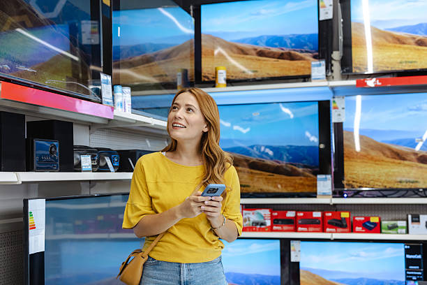 istock Smiling woman exploring electronics in a store while checking details on her phone 2217880716