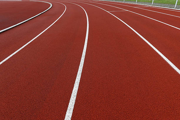 Empty red running track with white lines curving into the distance. Clean athletic stadium surface with no people. Sports background concept for competition, fitness, or motivation themes