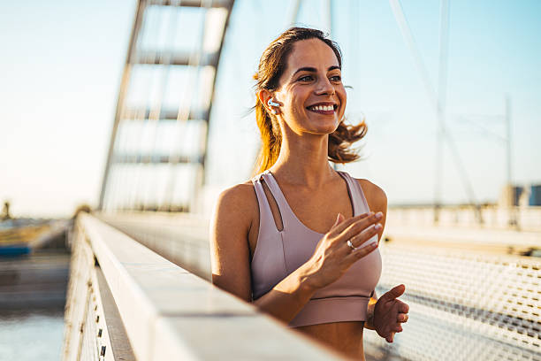 istock Smiling Woman Jogging on a Bridge with Wireless Earbuds on a Sunny Day 2217888224