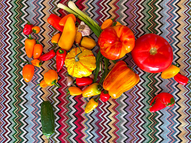 An assortment of colorful vegetables including tomatoes, peppers, and zucchini is artistically arranged on a vibrant textile in a sunny kitchen setting, showcasing freshness and abundance.
