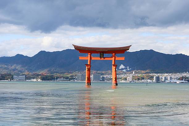 Itsukushima Shrine, Miyajimacho, Hatsukaichi, Hiroshima- 8 Dec 2024: red torii gate floating in the sea by the beach on a cloudy day