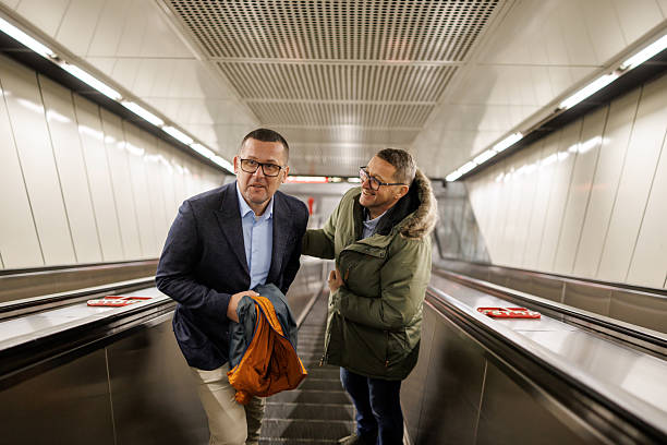Two mature male commuters chatting while moving up the subway escalator after work