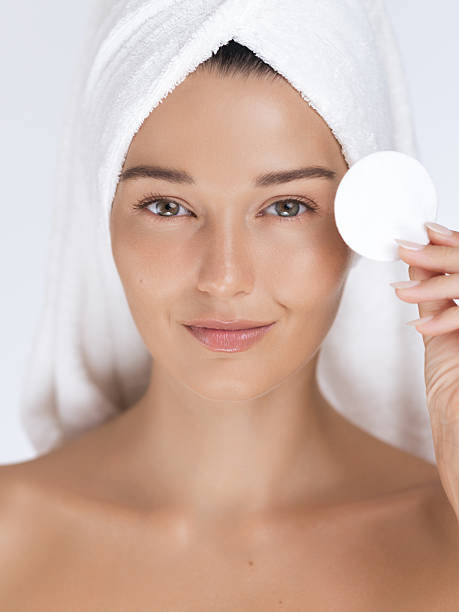 mujer con toalla sosteniendo almohadilla de algodón a ojo en concepto limpio de cuidado de la piel - mujeres-de-banners-verticales fotografías e imágenes de stock
